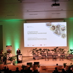 Na zdjęciu Wicemarszałek Województwa Śląskiego Leszek Pietraszek otwiera II Śląskie Forum Sprawiedliwej Transformacji. Widoczny jest ekran ze slajdem informującym, że organizatorem II Śląskiego Forum Sprawiedliwej Transformacji jest Departament Rozwoju i Transformacji Regionu Urzędu Marszałkowskiego Województwa Śląskiego. Na scenie są fotele dla panelistów, małe stoliczki, w tle - baner Regionalnego Obserwatorium Procesu Transformacji oraz kwiaty doniczkowe.