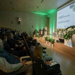 Na zdjęciu Wicemarszałek Województwa Śląskiego Leszek Pietraszek otwiera II Śląskie Forum Sprawiedliwej Transformacji. Prowadząca Forum stoi w tyle. Widoczny jest ekran ze slajdem informującym, że organizatorem II Śląskiego Forum Sprawiedliwej Transformacji jest Departament Rozwoju i Transformacji Regionu Urzędu Marszałkowskiego Województwa Śląskiego. Na scenie są fotele dla panelistów, małe stoliczki, w tle - baner Regionalnego Obserwatorium Procesu Transformacji oraz kwiaty doniczkowe. Na zdjęciu widać także część widowni wraz z uczestnikami - rzut z boku.