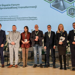 Na zdjęciu jest sześciu prelegentów i moderator Panelu 3 stojący na scenie i pozujący do zdjęcia. W tle slajd informujący, że organizatorem II Śląskiego Forum Sprawiedliwej Transformacji jest Departament Rozwoju i Transformacji Regionu Urzędu Marszałkowskiego Województwa Śląskiego. 
