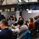 Spotkanie w przestrzeni poprzemysłowej: uczestnicy przy stołach, w tle metalowa konstrukcja i ceglane ściany