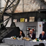 Spotkanie w przestrzeni poprzemysłowej: uczestnicy przy stołach, w tle metalowa konstrukcja i ceglane ściany