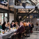 Spotkanie w przestrzeni poprzemysłowej: uczestnicy przy stołach, w tle metalowa konstrukcja i ceglane ściany