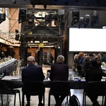 Spotkanie w przestrzeni poprzemysłowej: uczestnicy przy stołach, w tle metalowa konstrukcja i ceglane ściany