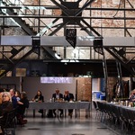 Spotkanie w przestrzeni poprzemysłowej: uczestnicy przy stołach, w tle metalowa konstrukcja i ceglane ściany