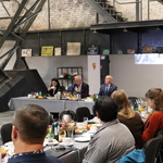 Spotkanie w przestrzeni poprzemysłowej: uczestnicy przy stołach, w tle metalowa konstrukcja i ceglane ściany