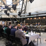 Spotkanie w przestrzeni poprzemysłowej: uczestnicy przy stołach, w tle metalowa konstrukcja i ceglane ściany