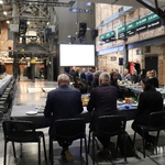 Spotkanie w przestrzeni poprzemysłowej: uczestnicy przy stołach, w tle metalowa konstrukcja i ceglane ściany