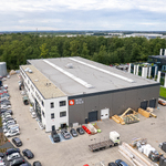 Widok z lotu ptaka na kompleks produkcyjno-magazynowy firmy BOX HAUS z halami, parkingami, składowanymi materiałami oraz otaczającymi terenami zielonymi.