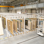 Wnętrze hali produkcyjnej firmy BOX HAUS z liniami technologicznymi do obróbki drewna, składowanymi elementami konstrukcyjnymi, wózkiem widłowym oraz suwnicą pomostową.